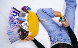 Person sitting on a bed with a cocktail, next to a gift basket