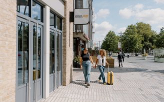 Two people walking outside YOTEPAD London Stratford on a sunny day, with a suitcase and looking us at the YOTELPAD sign